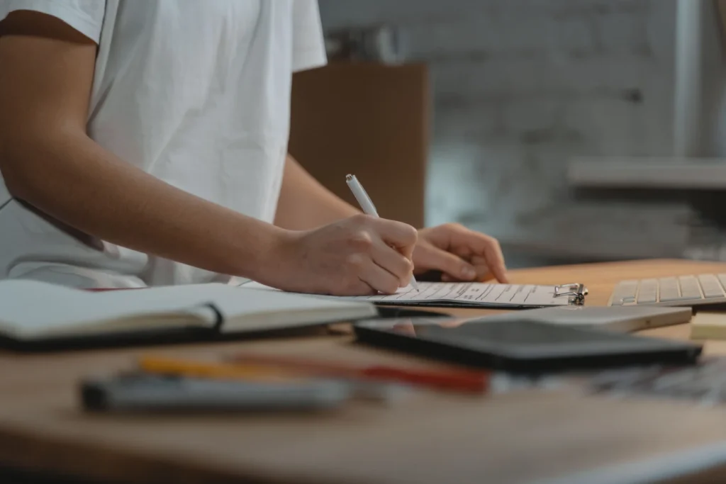 Persona escribiendo una lista de documentos en un portapapeles sobre un escritorio