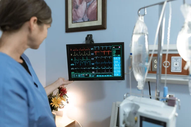 Enfermera con uniforme azul revisando un monitor de signos vitales